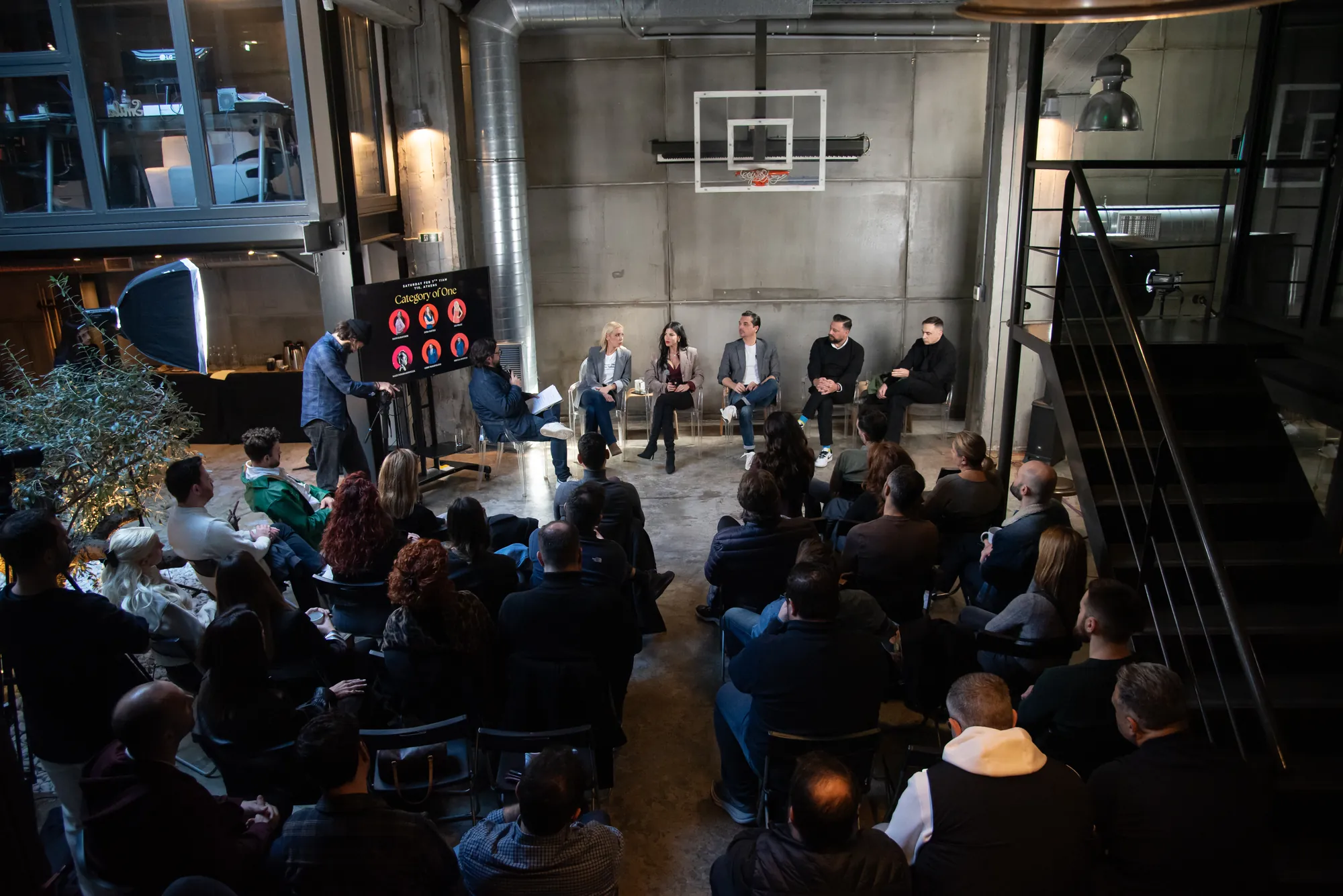 Wide view of the full audience seated around the panel in the industrial venue